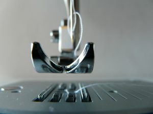 a sewing machine presser foot raised with white thread